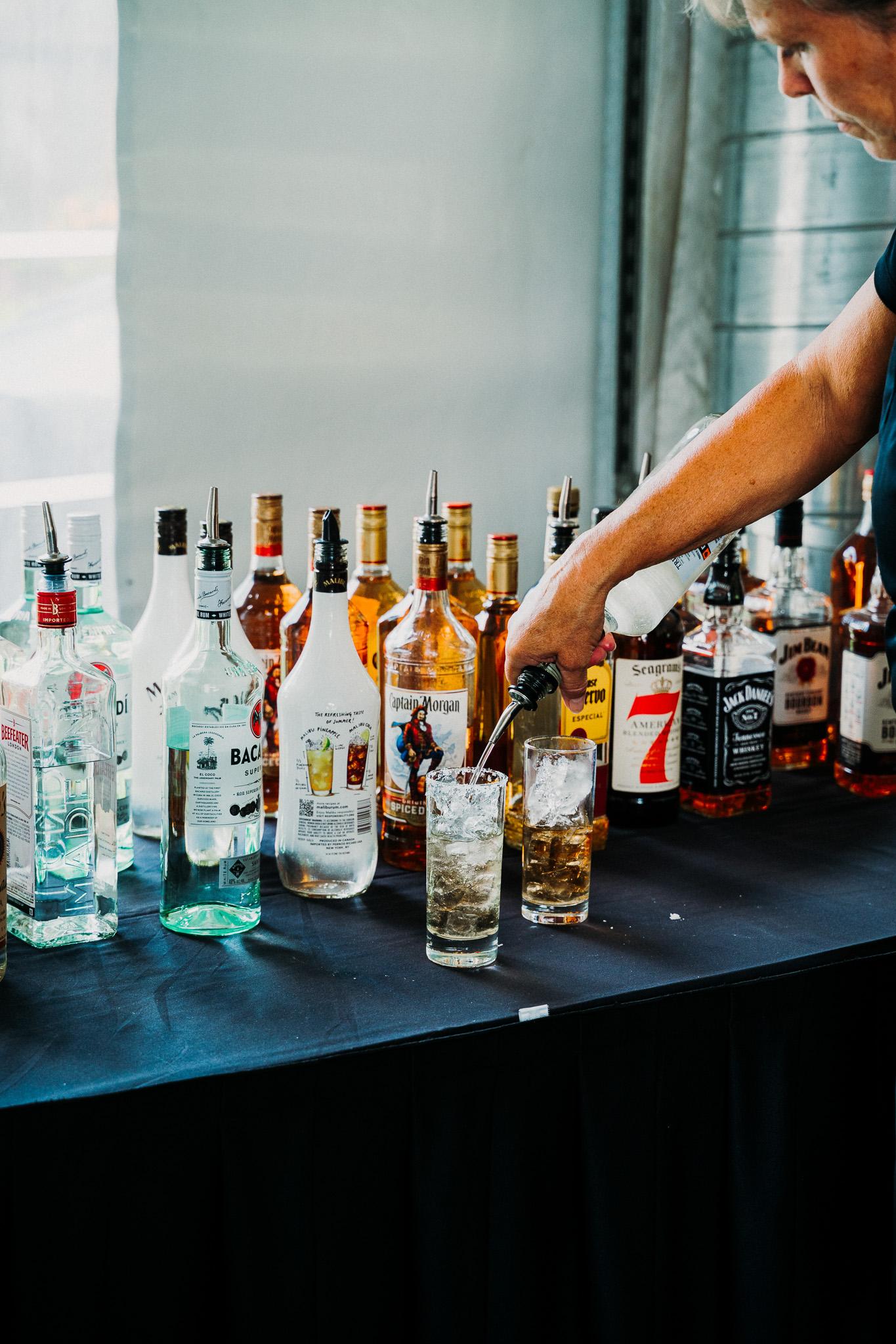 Various liquor bottles on a table, person pouring into a glass.