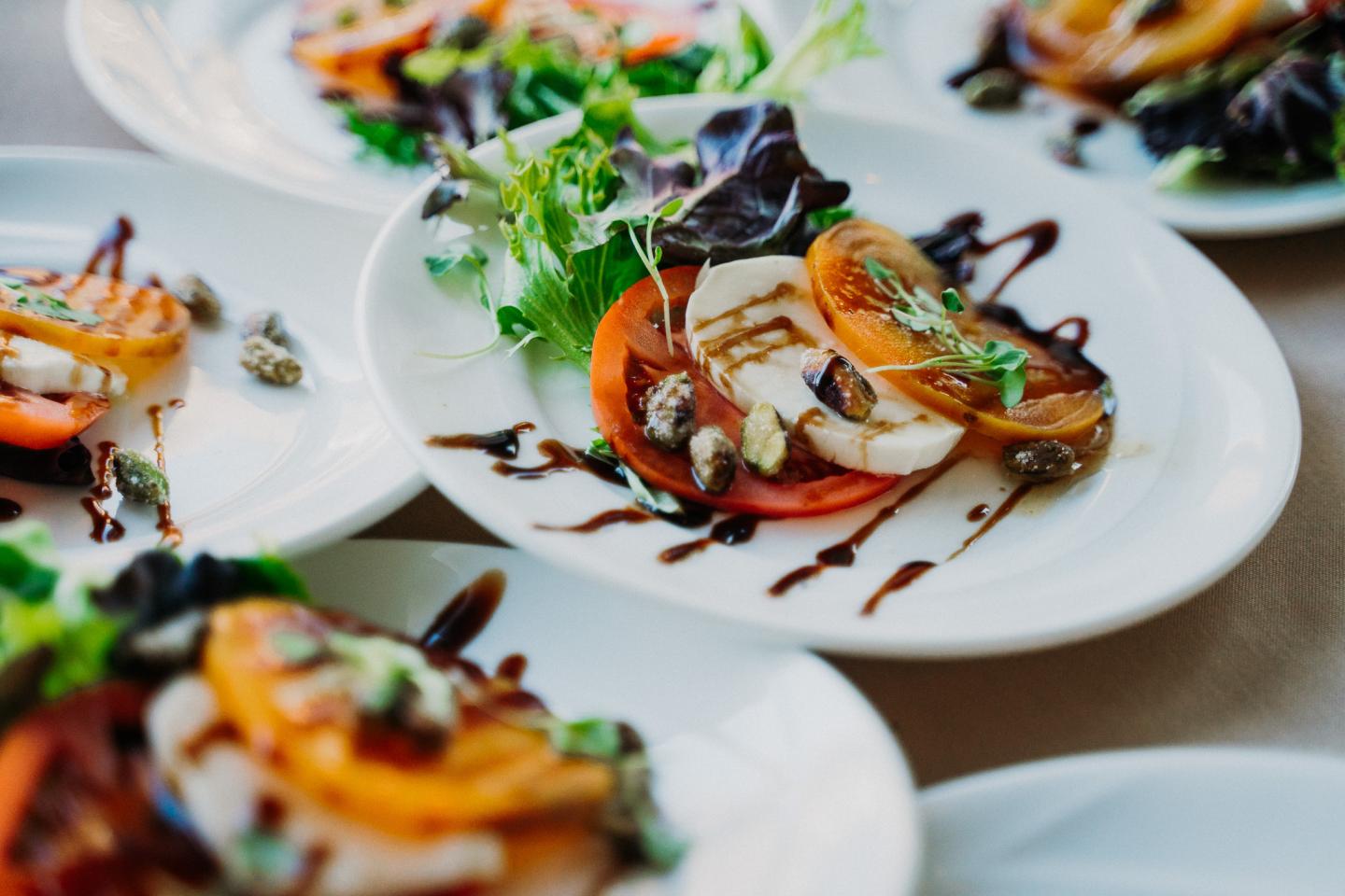 Caprese salad with tomatoes, mozzarella, and greens on white plates.