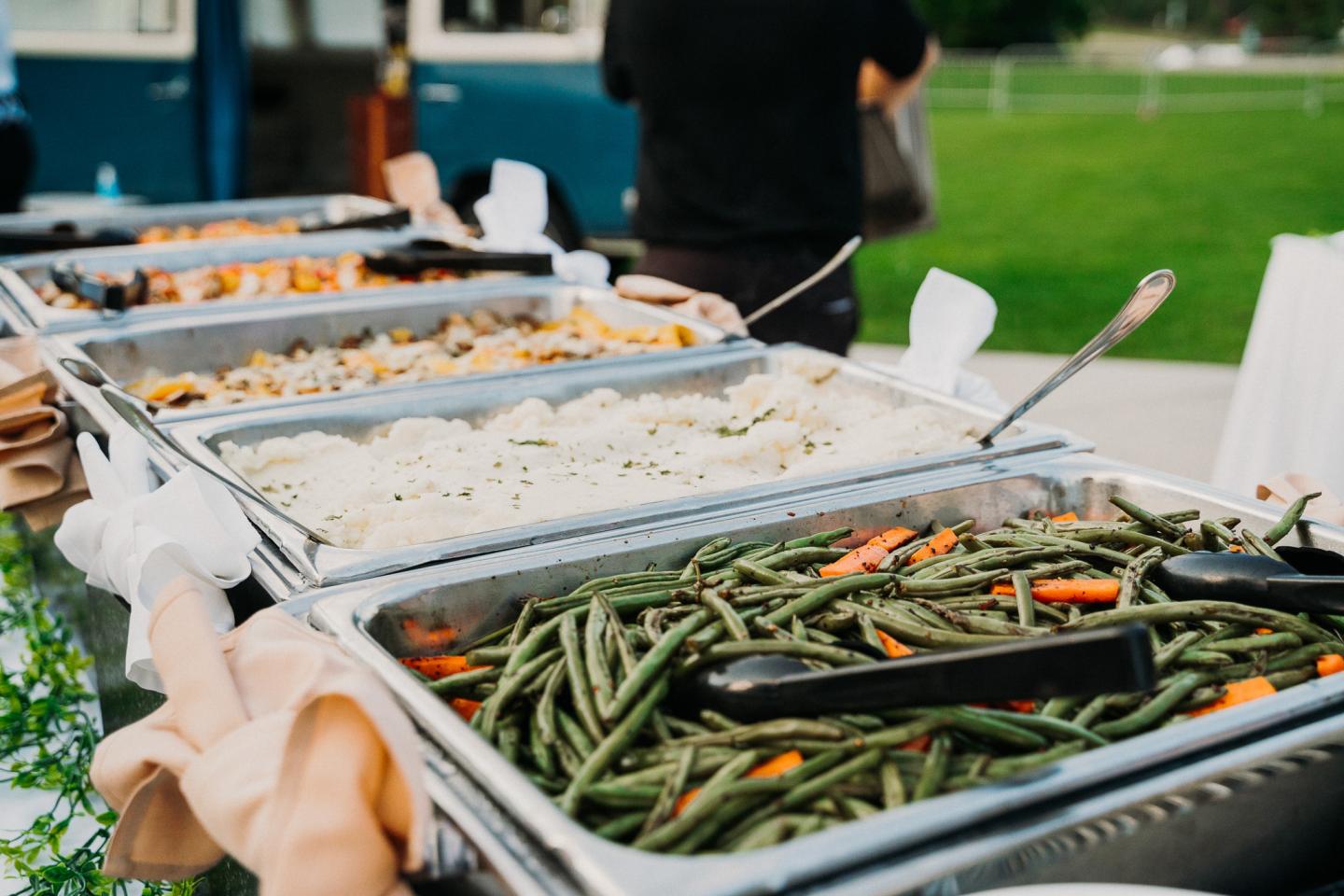 Buffet table with trays of rice and green beans outdoors.