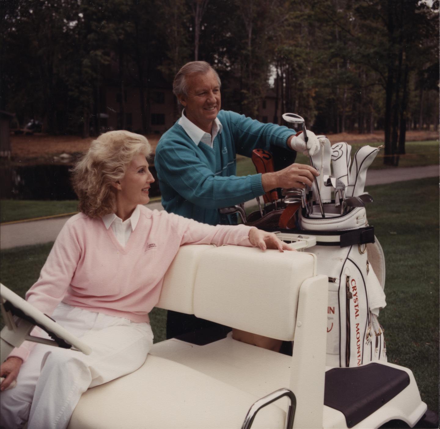 Man and woman with golf cart, smiling and organizing clubs outdoors.
