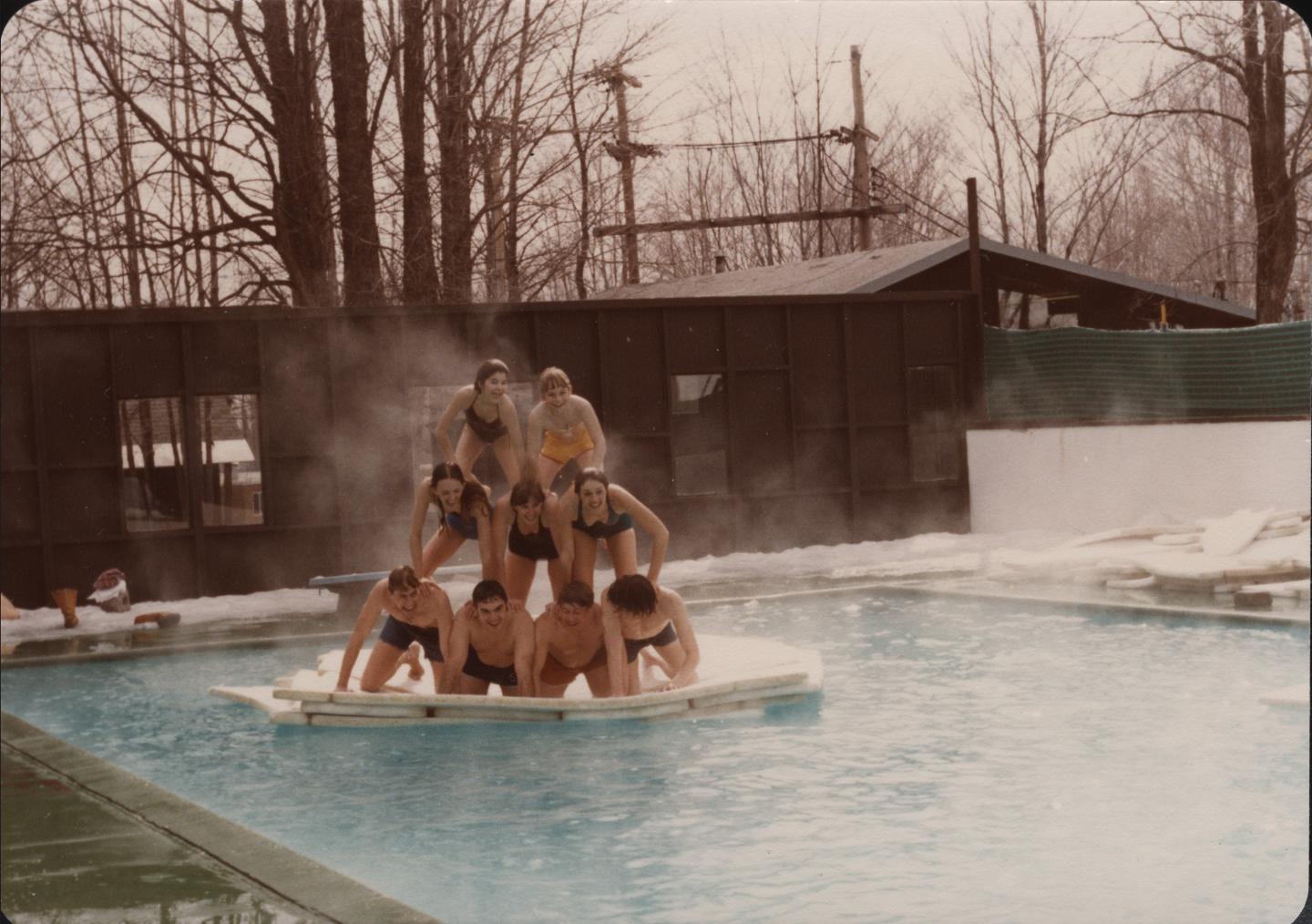 People forming a human pyramid on a floating mat in an outdoor pool.