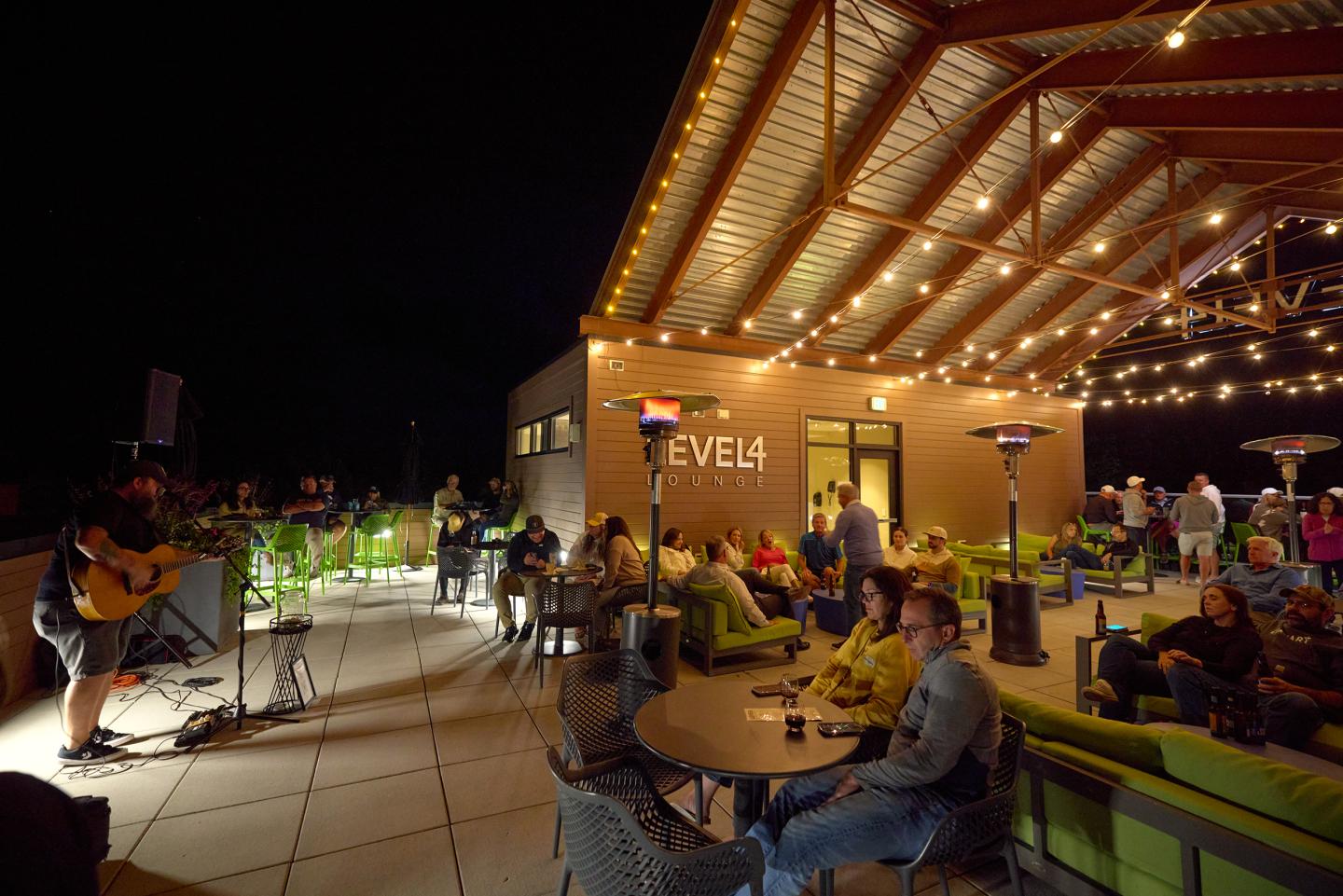 Patio at night with string lights, people relaxing, guitarist performing.