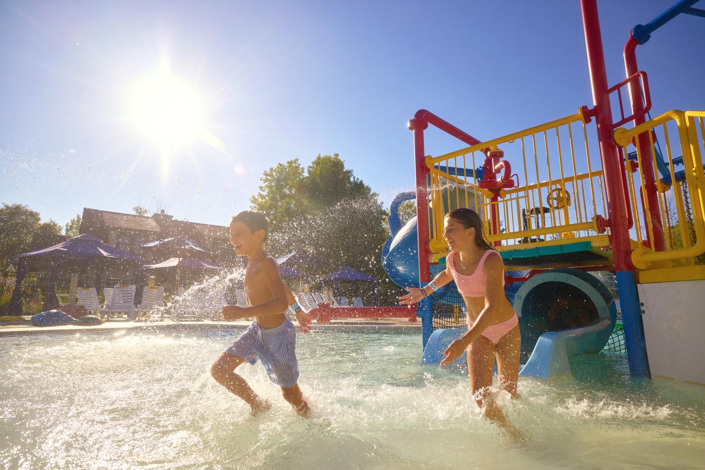 Children playing in a sunny water park, splashing near colorful slides.
