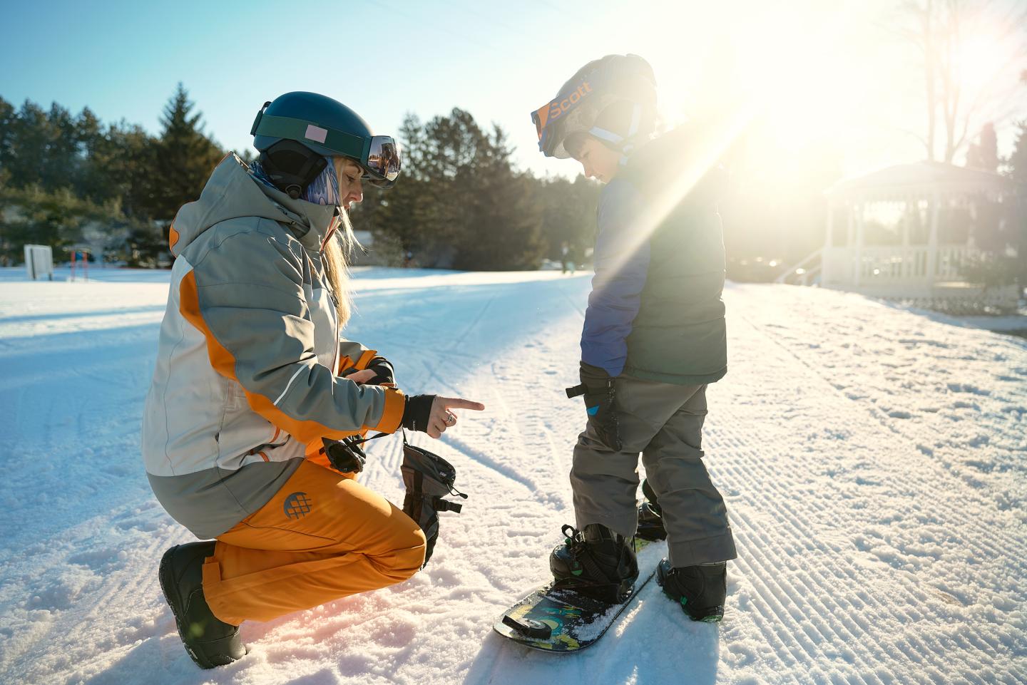 A child and adult in ski gear on a sunny snowy slope.