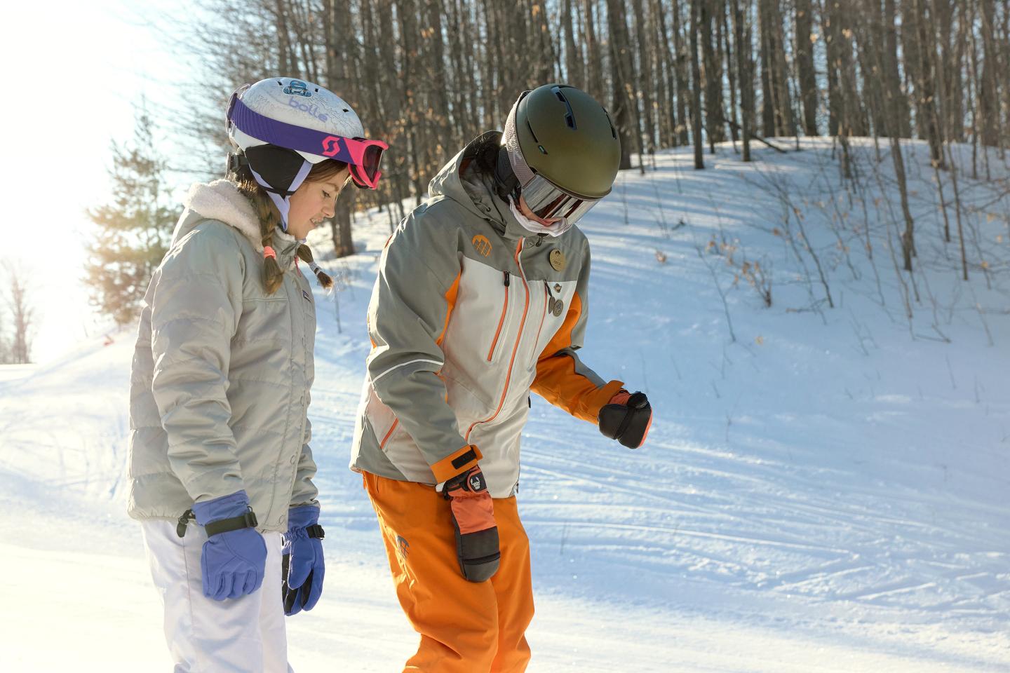 Two people skiing on a snowy slope, wearing helmets and winter gear.