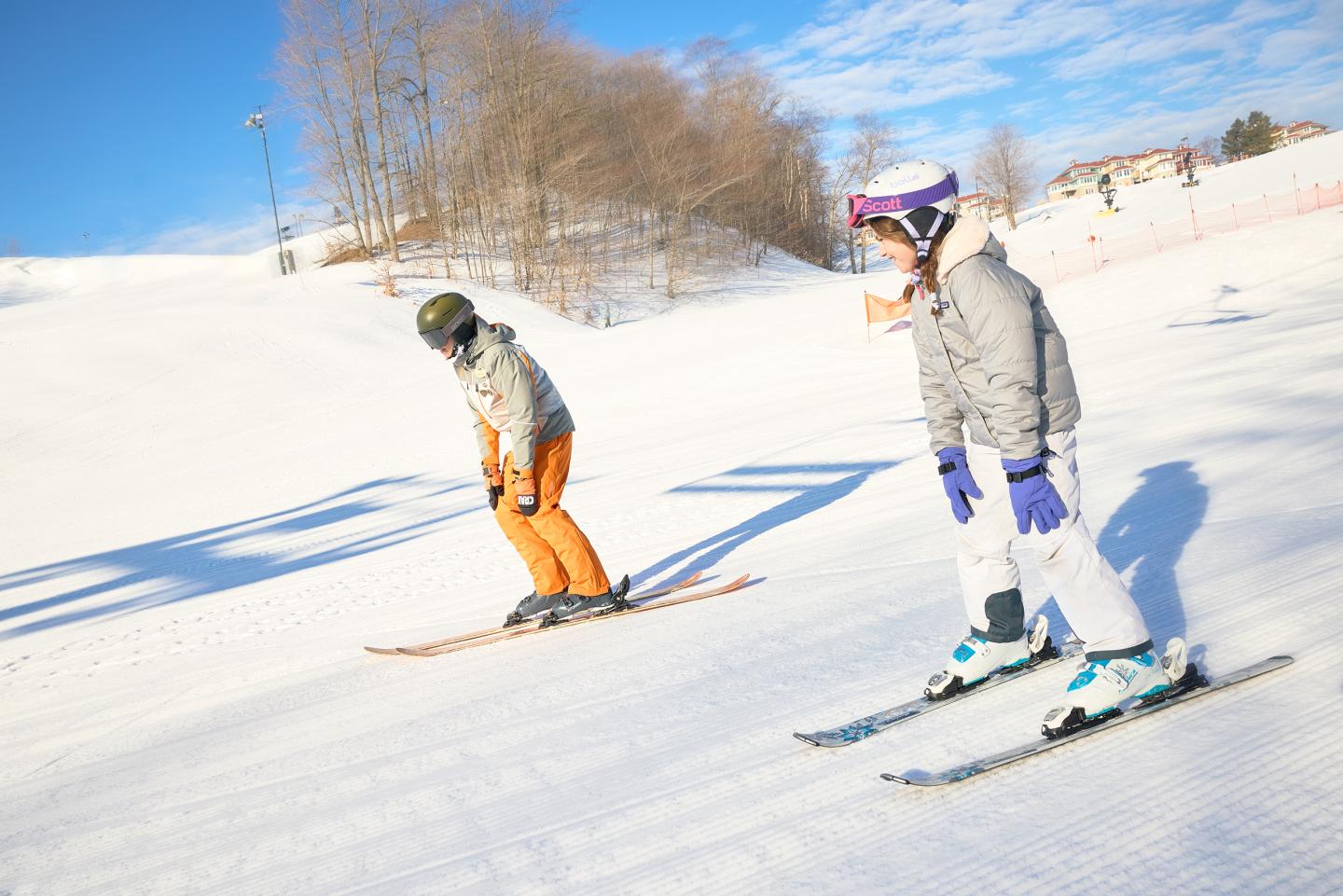 Two skiers in winter gear on a snowy slope, under a clear blue sky.
