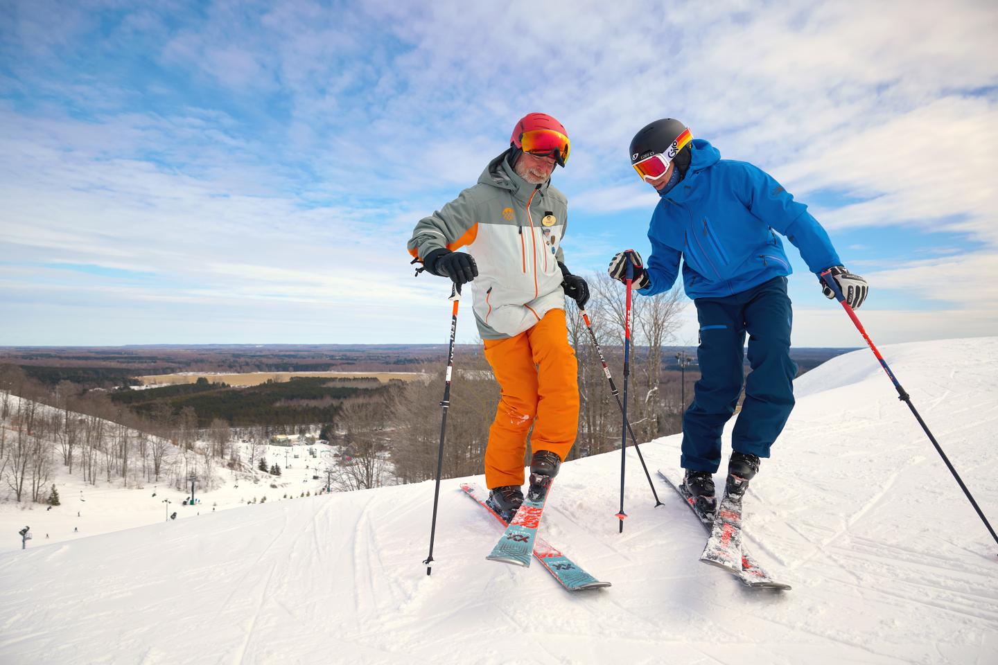 Two people skiing on a snowy slope under a blue sky.