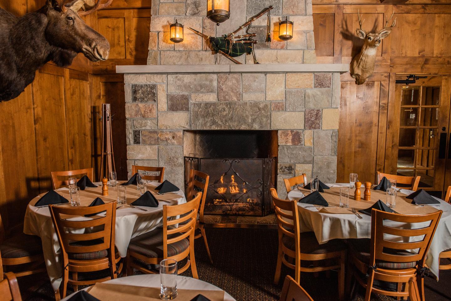 Rustic dining room with a stone fireplace, round tables, and wooden chairs.
