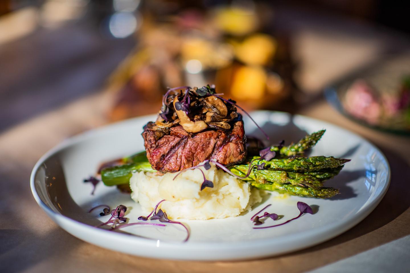 Steak on mashed potatoes with asparagus and mushroom garnish.