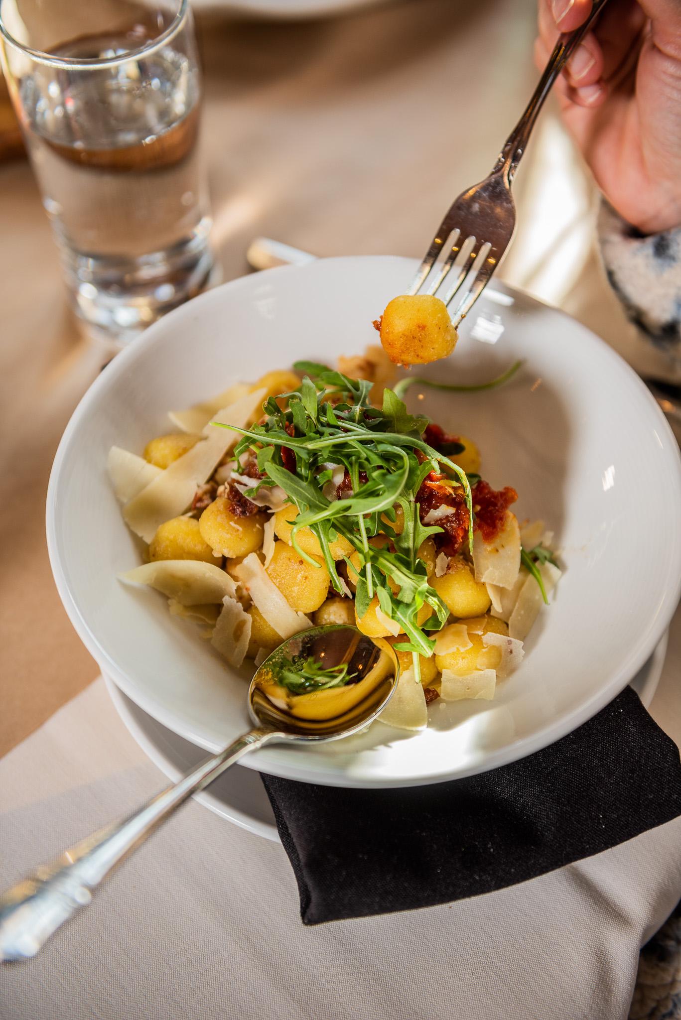 Gnocchi in a white bowl with greens and sundried tomatoes, fork lifting a piece.
