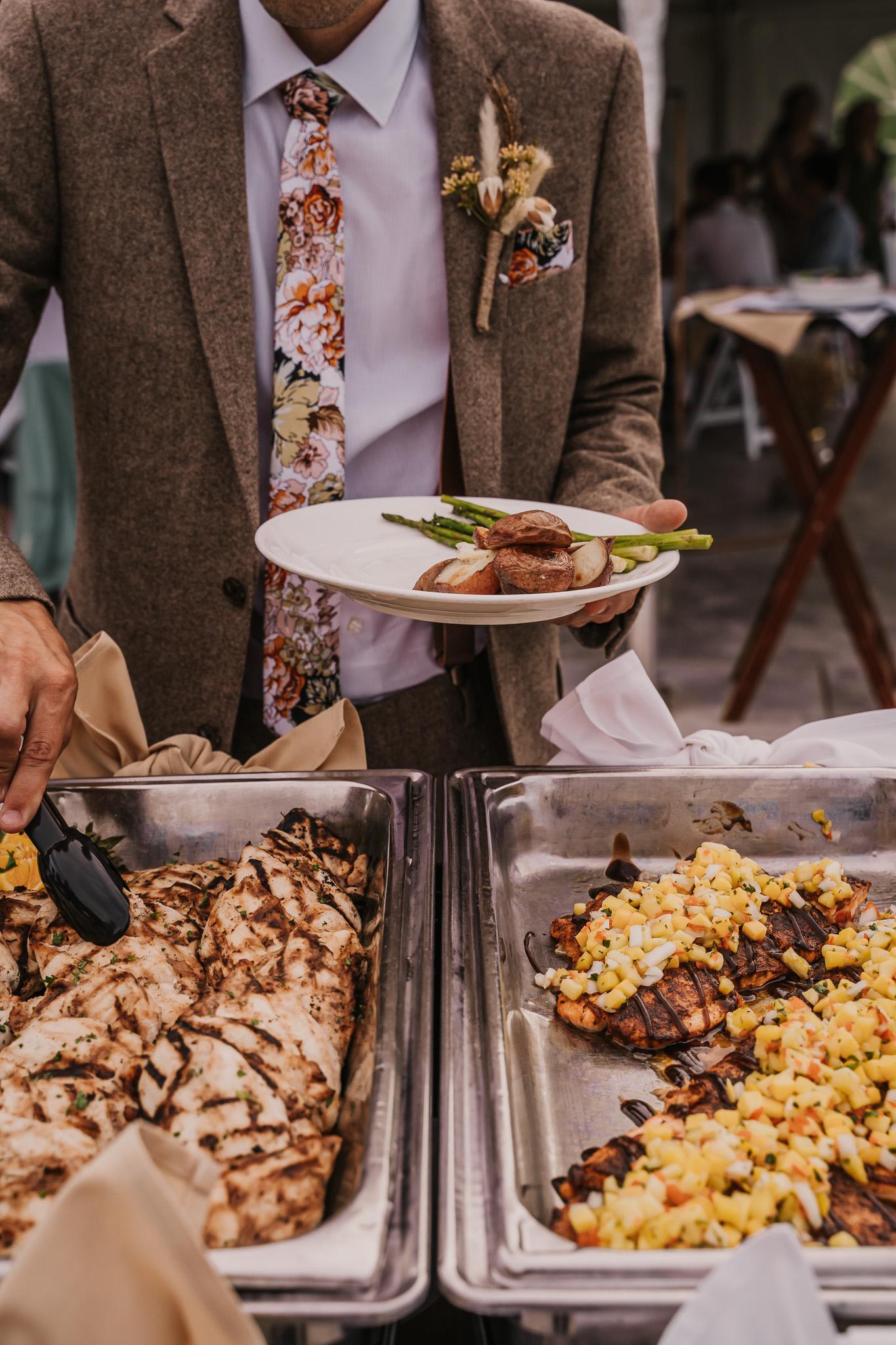 Man in suit holding plate near buffet trays with decorated dishes.