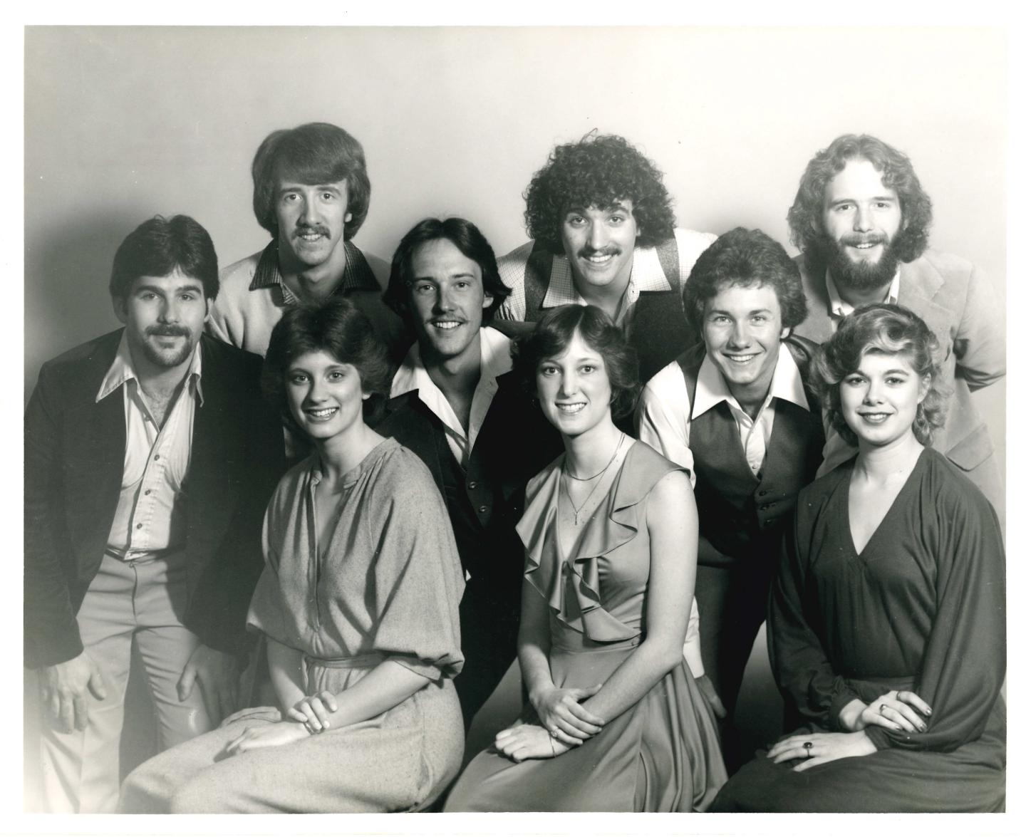 Group of eight people smiling in a vintage black and white photograph.