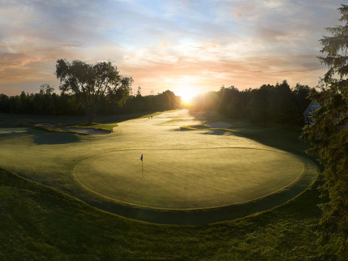 Sunrise over a lush, green golf course with a flag on the putting green.