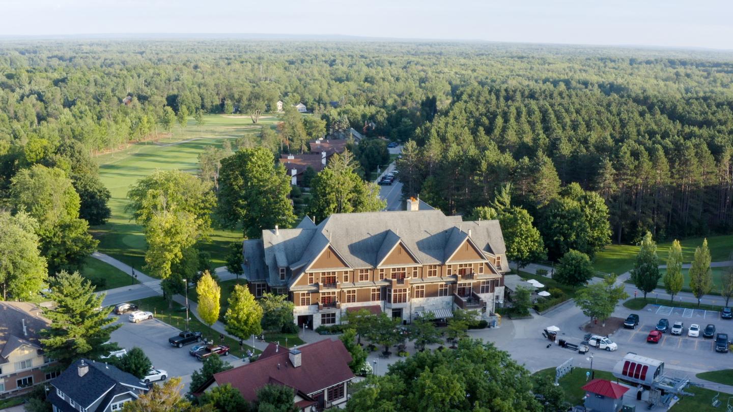 Aerial view of a large rustic building surrounded by trees and a golf course.