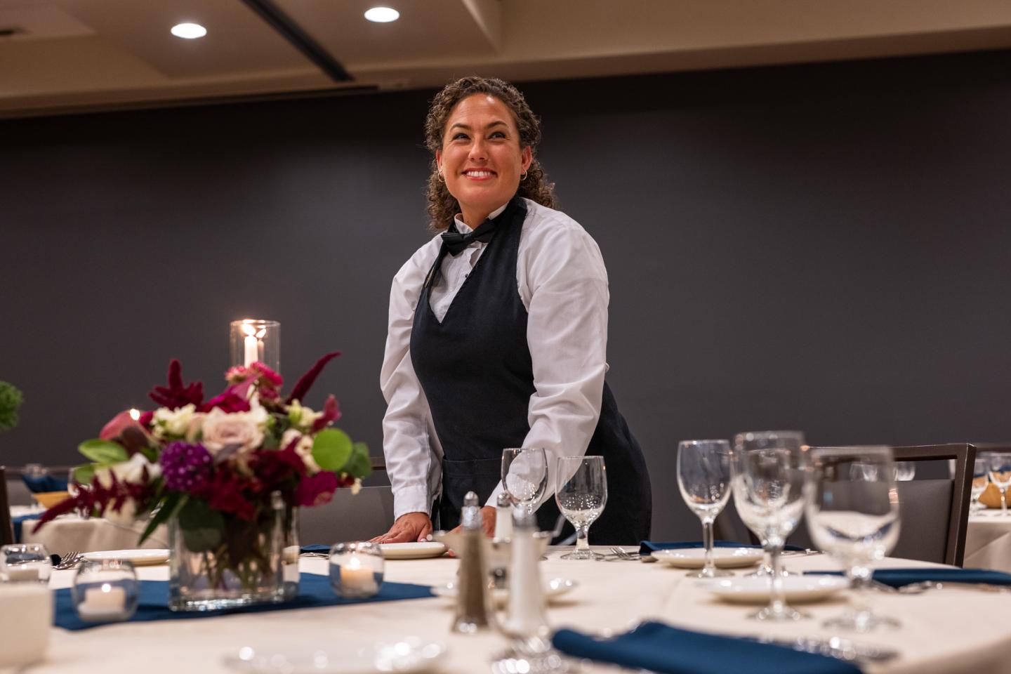 Server in uniform setting an elegant dining table.