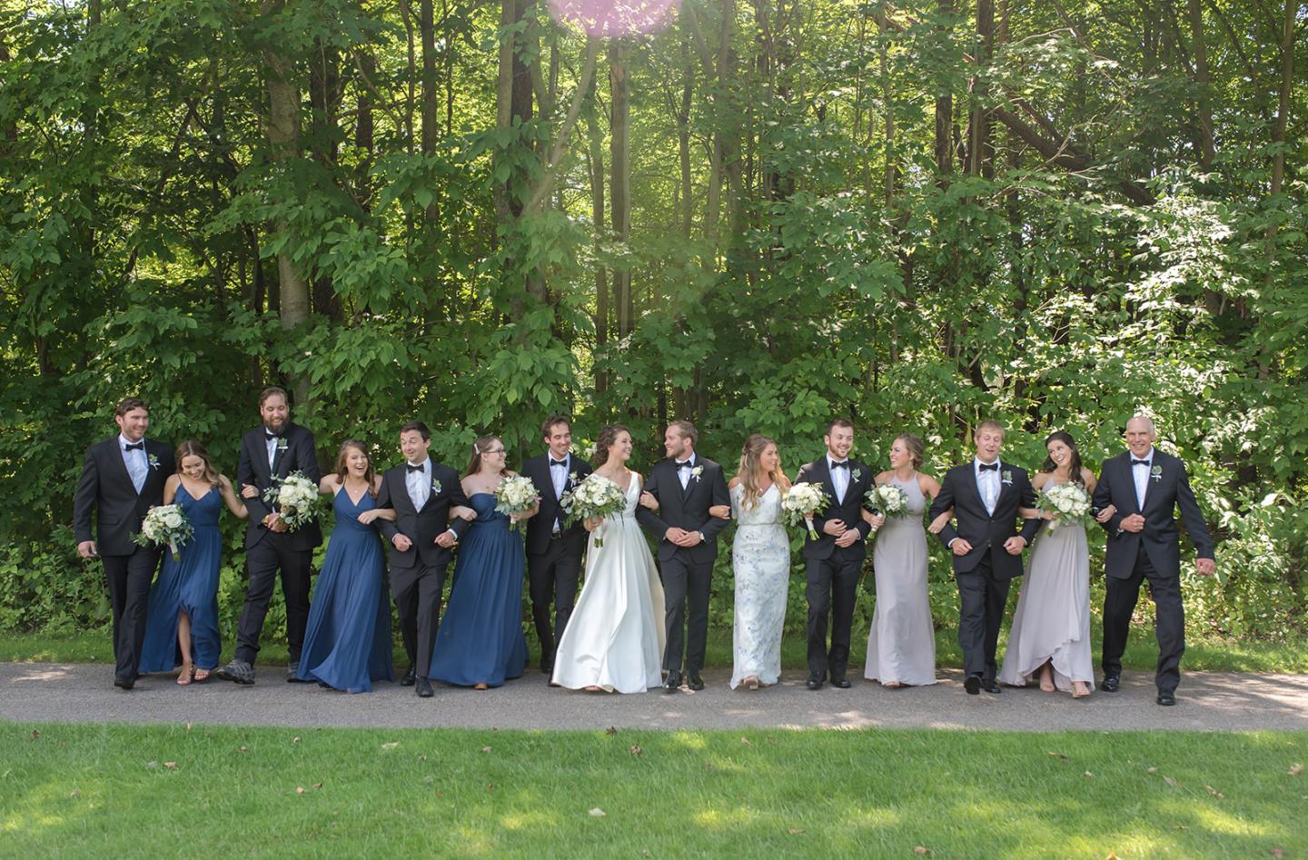 Wedding party in formal attire posing outdoors with trees in the background.
