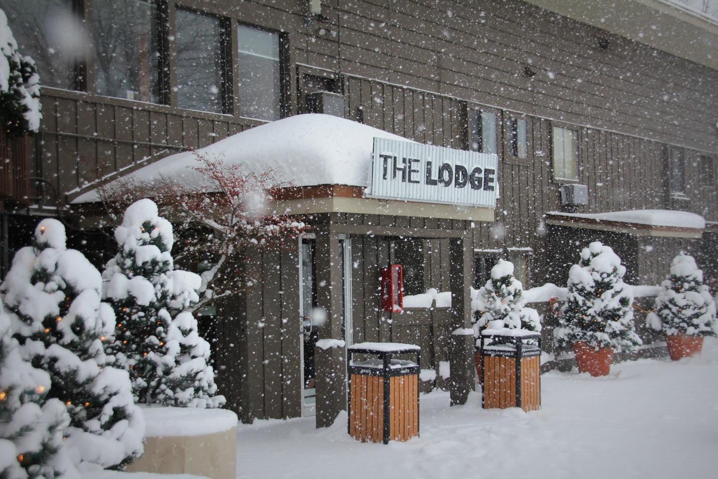 Snow-covered lodge entrance with decorated trees, heavy snowfall.
