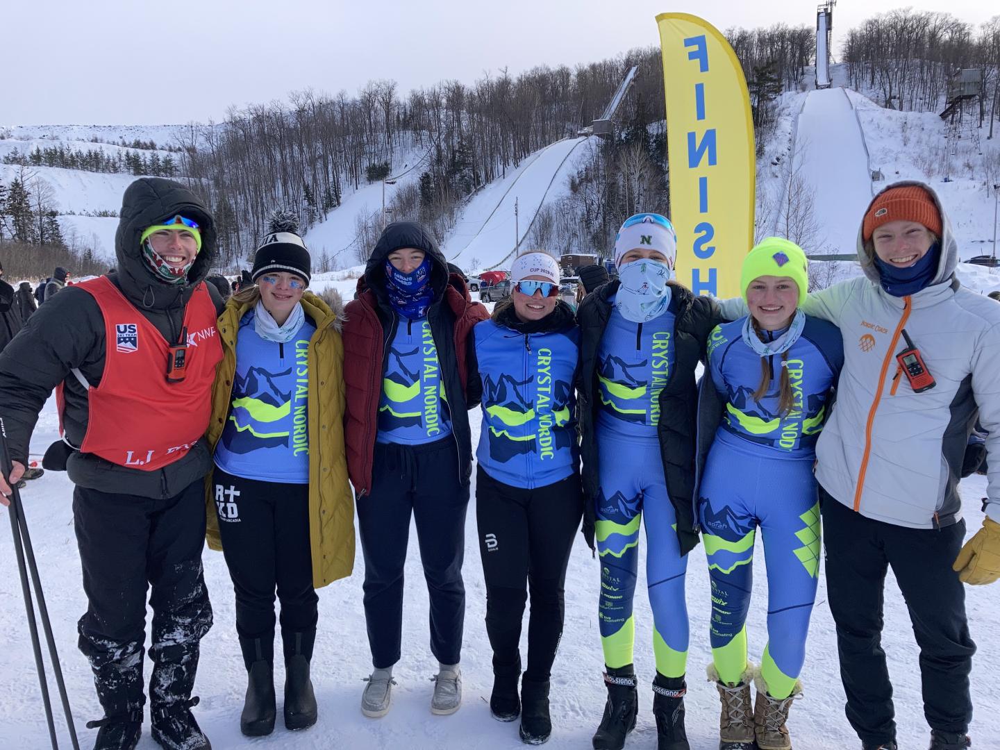 Group of people in winter gear smiling on snowy hill with finish flag in background.