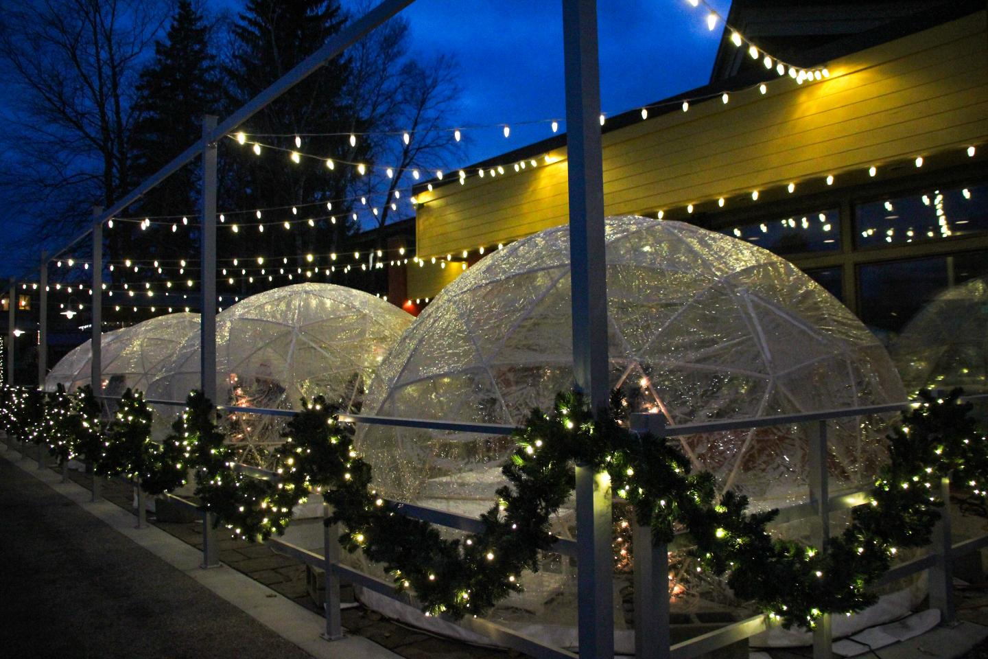 Outdoor restaurant domes lit with festive string lights at dusk.