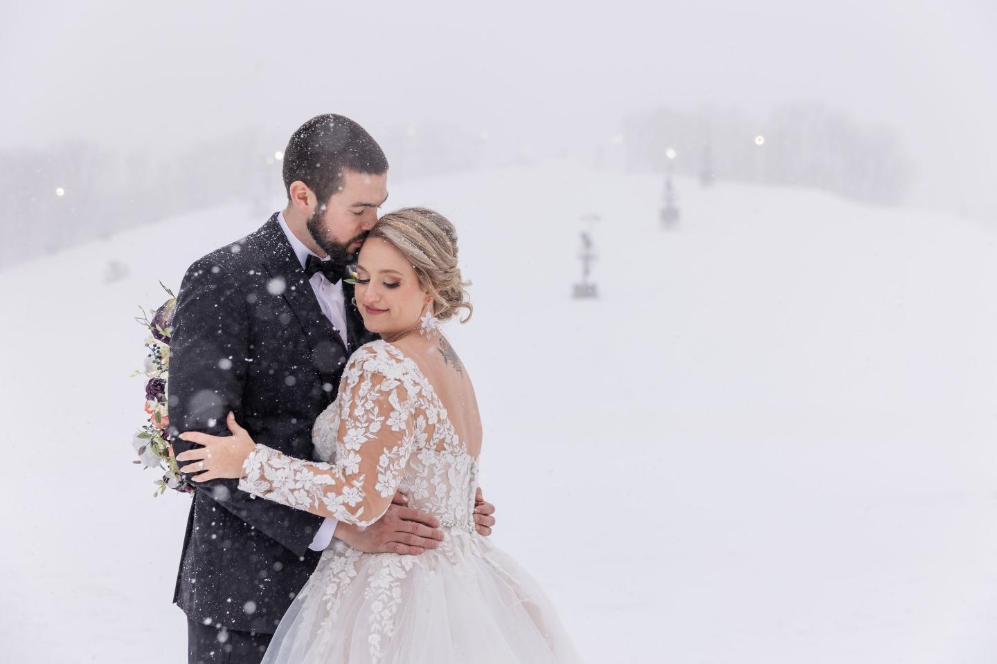 Couple embraces in snowy landscape, wearing wedding attire.