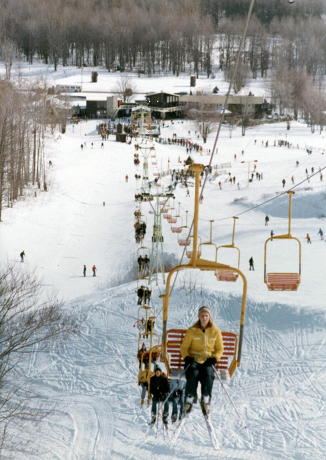 Ski lift ascending a snowy slope with people in winter clothing.