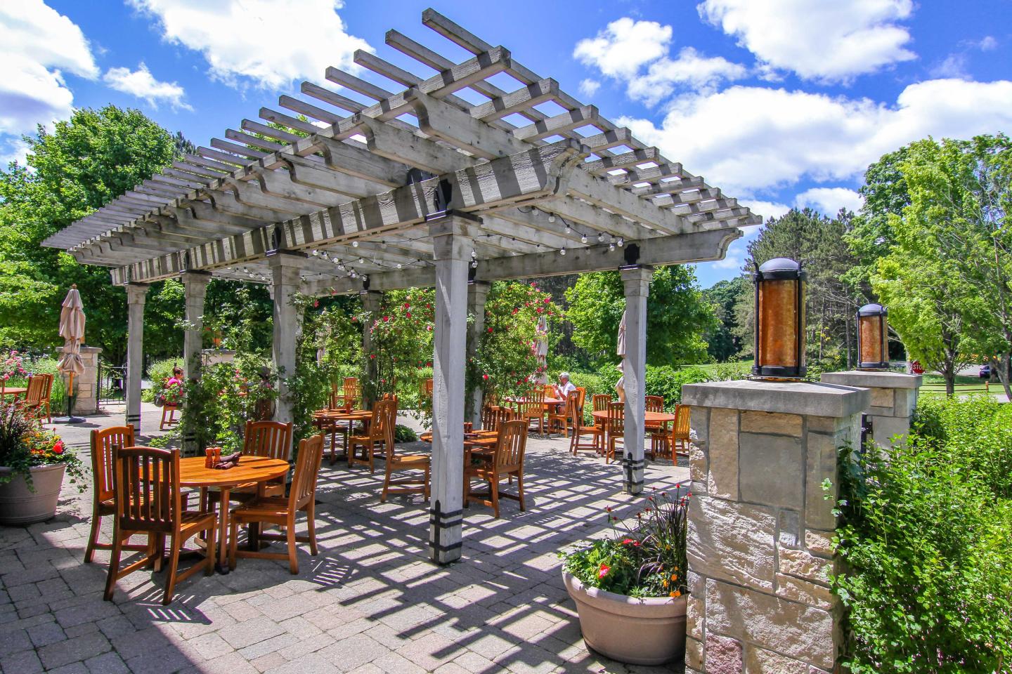 Outdoor patio with wooden pergola, tables, and chairs under a blue sky.