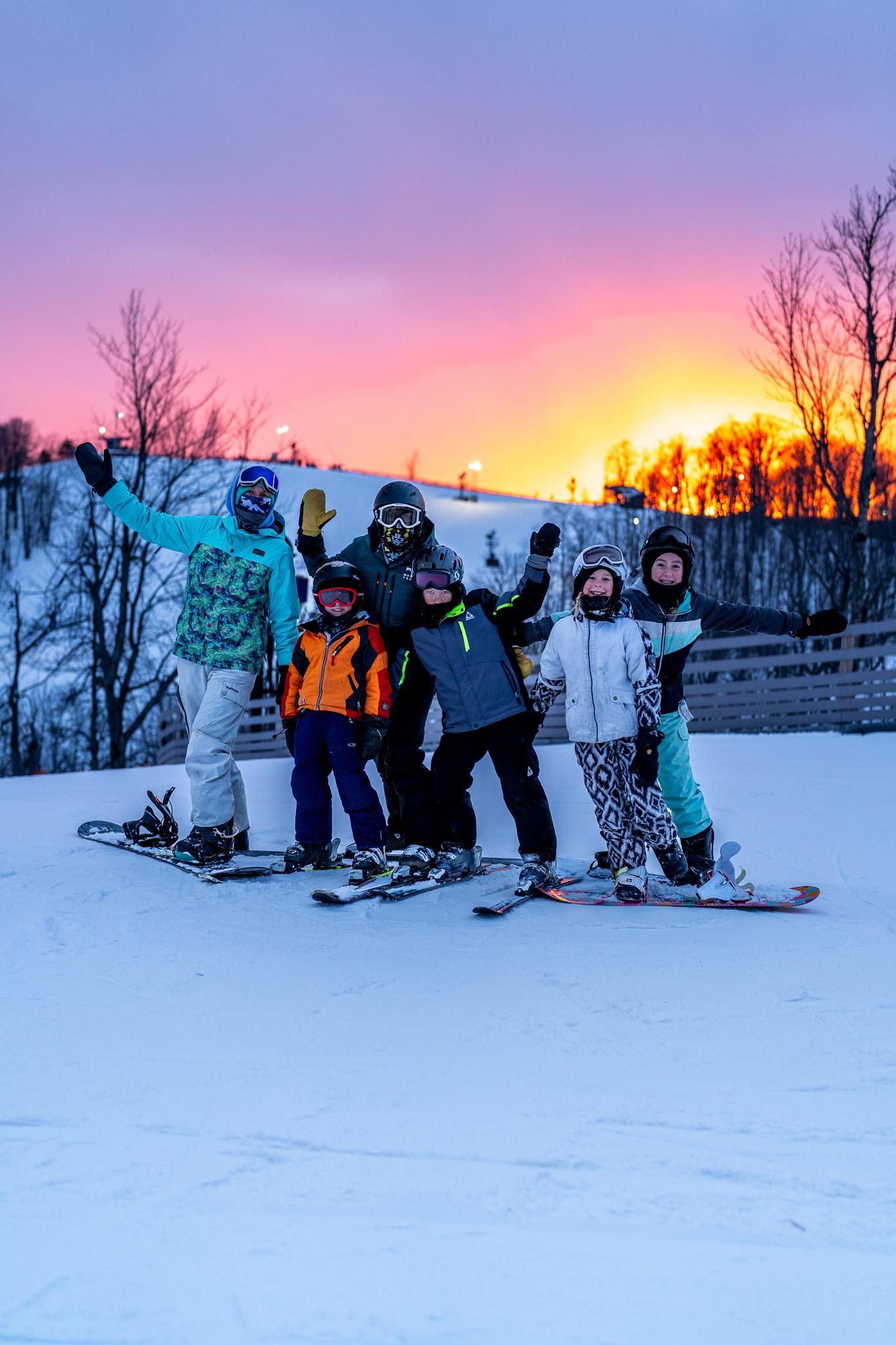 Skiers posing at sunset on a snowy slope, wearing colorful winter gear.