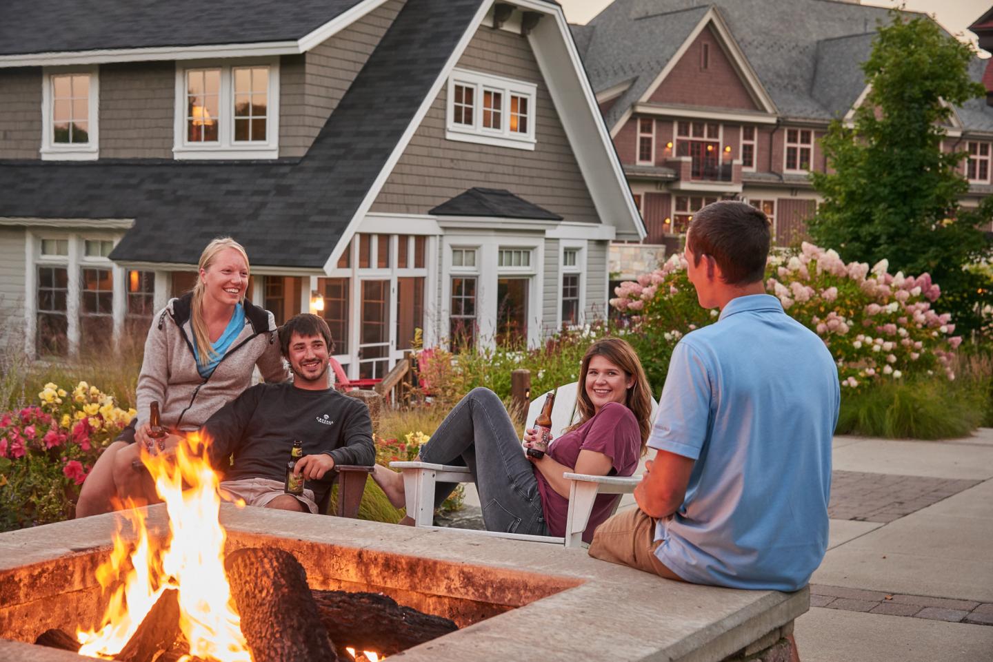 Four people smiling around a backyard fire pit at sunset.