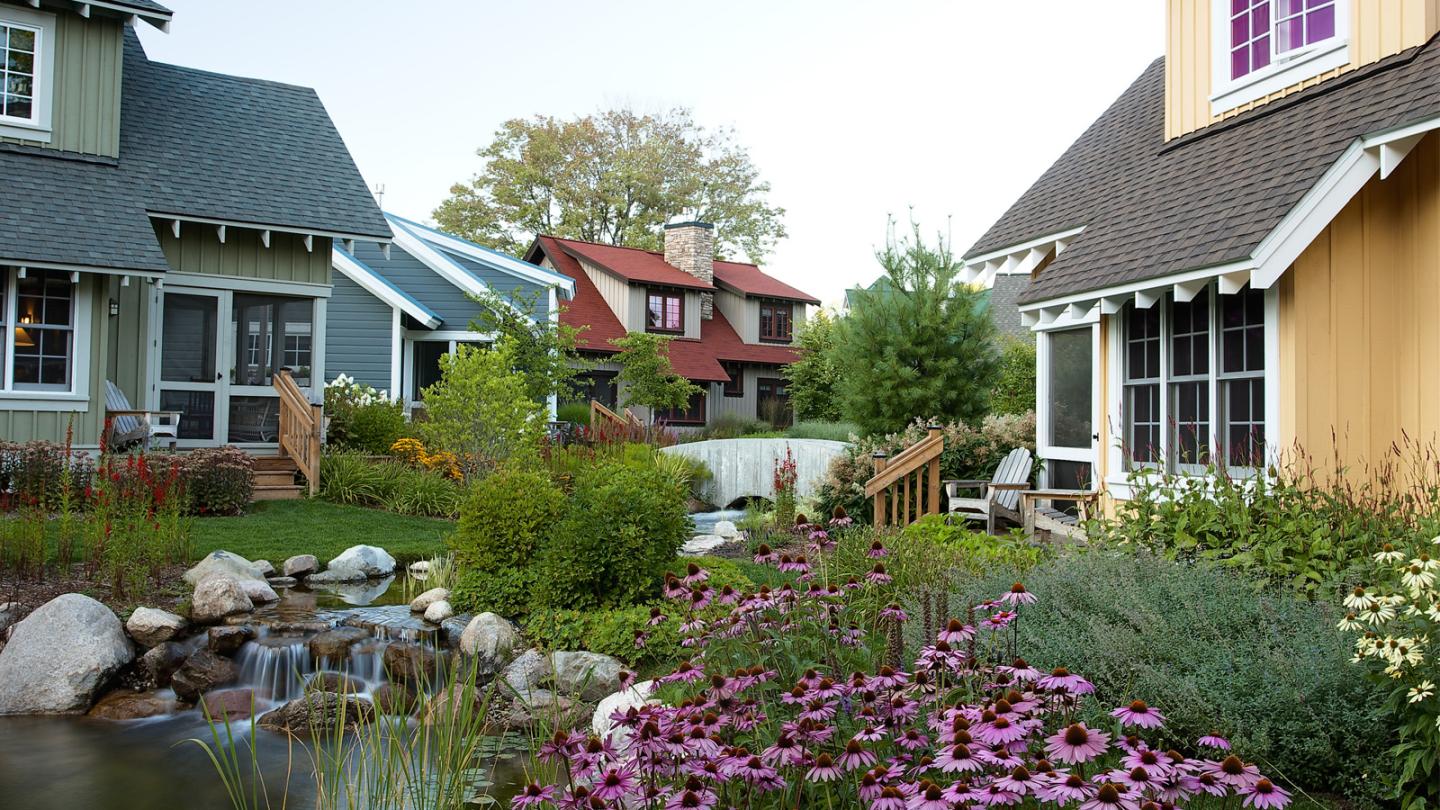 Cozy cottages with gardens, pond, and blooming flowers; serene neighborhood setting.