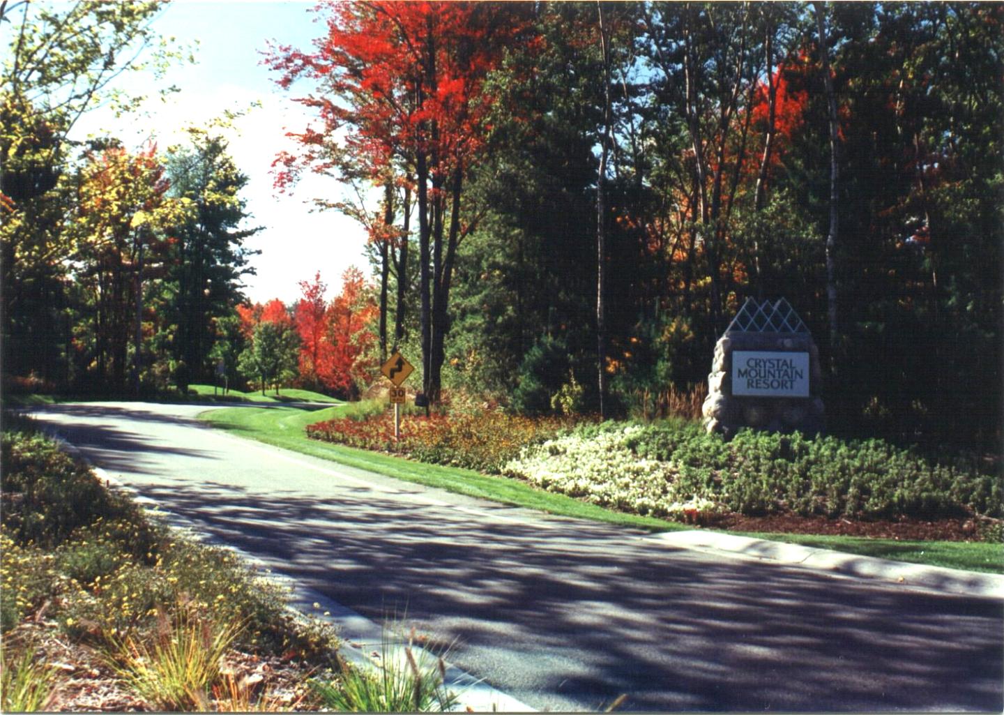 Curving road with colorful autumn trees and a stone sign on the right.