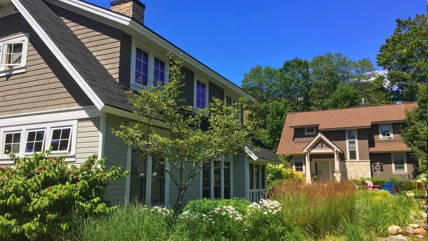 Two houses surrounded by lush greenery under a clear blue sky.