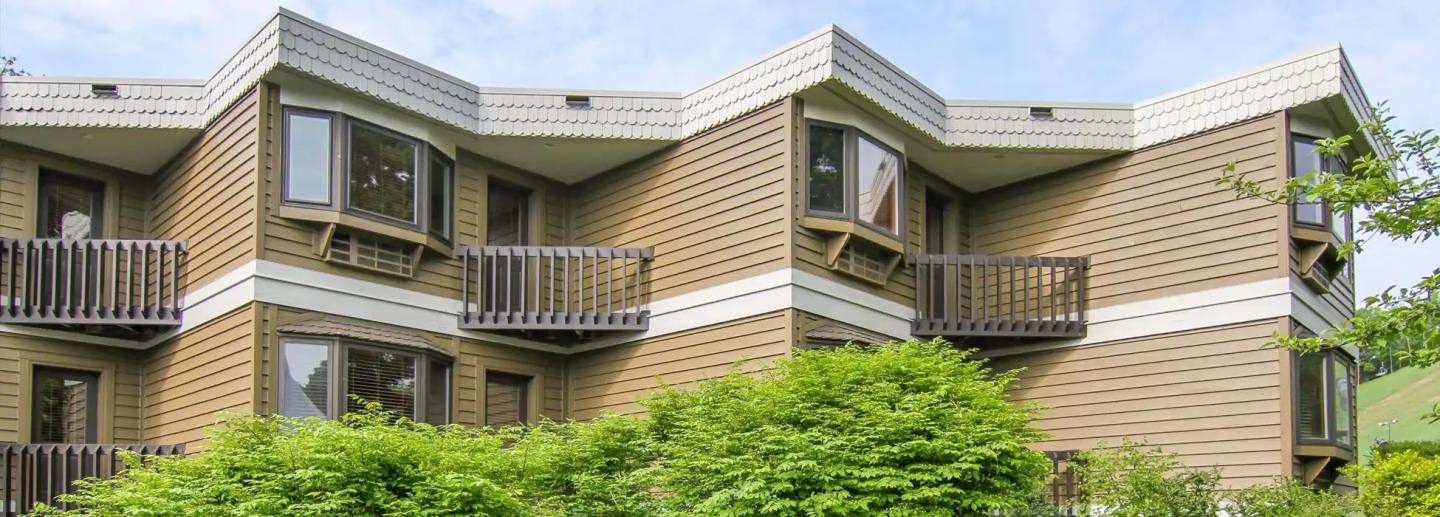 Brown building with zigzag design and balconies, surrounded by greenery.
