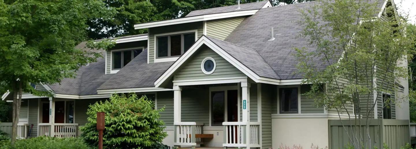 Two-story house with gray siding and a front porch, surrounded by greenery.
