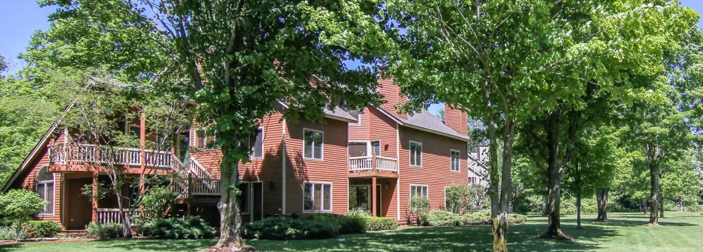 Red brick house surrounded by trees and greenery.