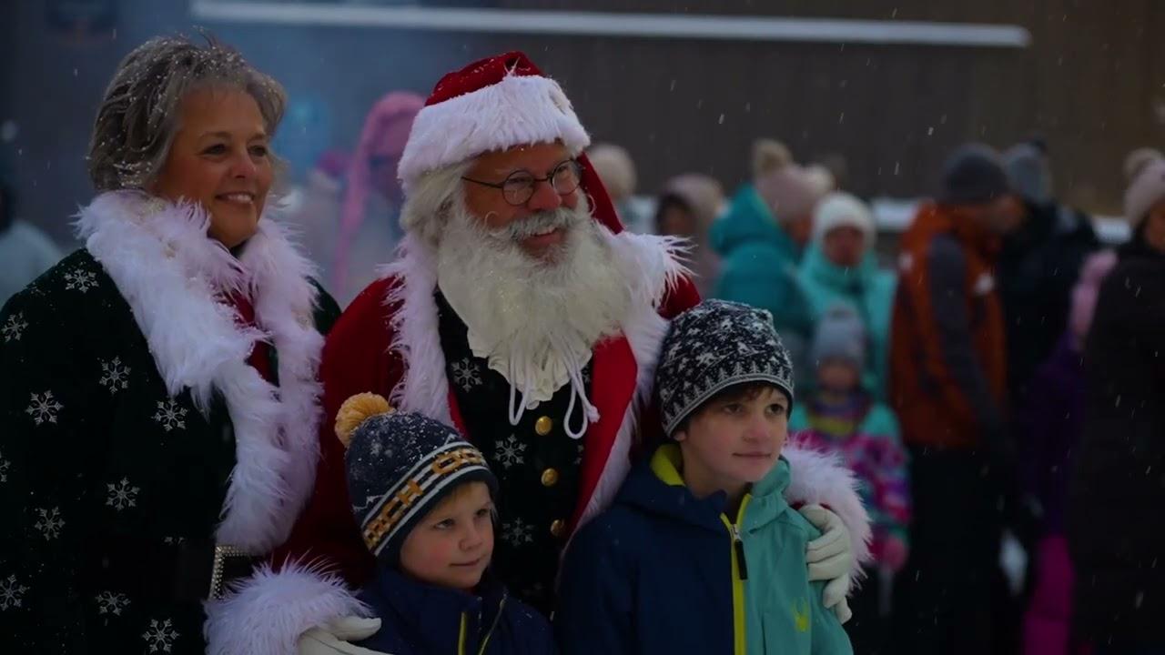 Santa and Mrs. Claus with two children in winter coats and hats at an outdoor event.
