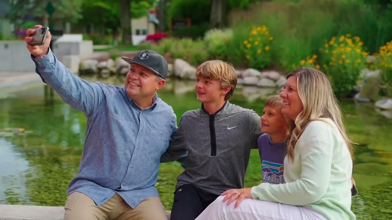 Family taking a selfie by a pond, smiling and sitting closely together.