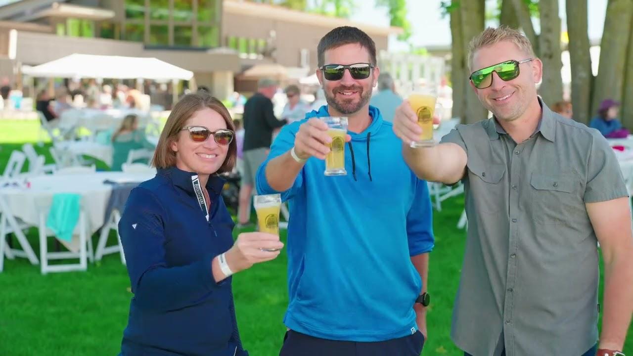 Three people in sunglasses toast with drinks at an outdoor event on a sunny day.