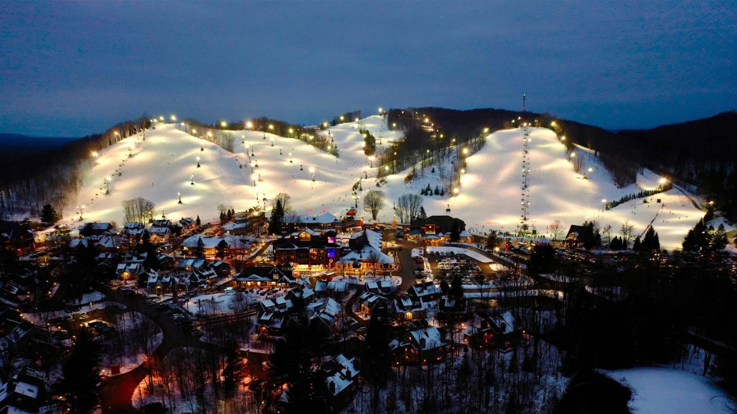 Ski slopes lit up at night, surrounded by a snowy village.