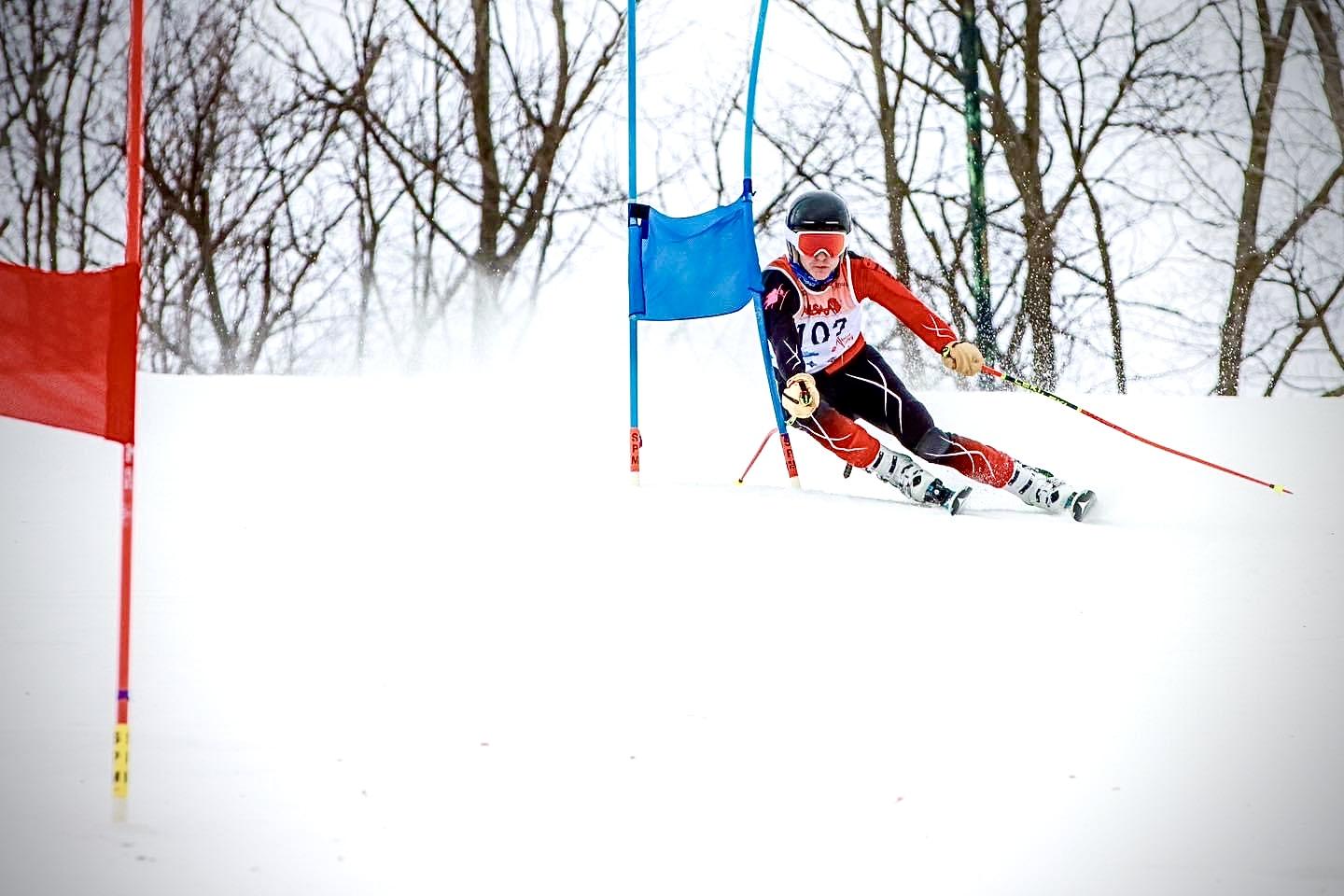 Skier in action on a snowy slope, passing between red and blue flags.