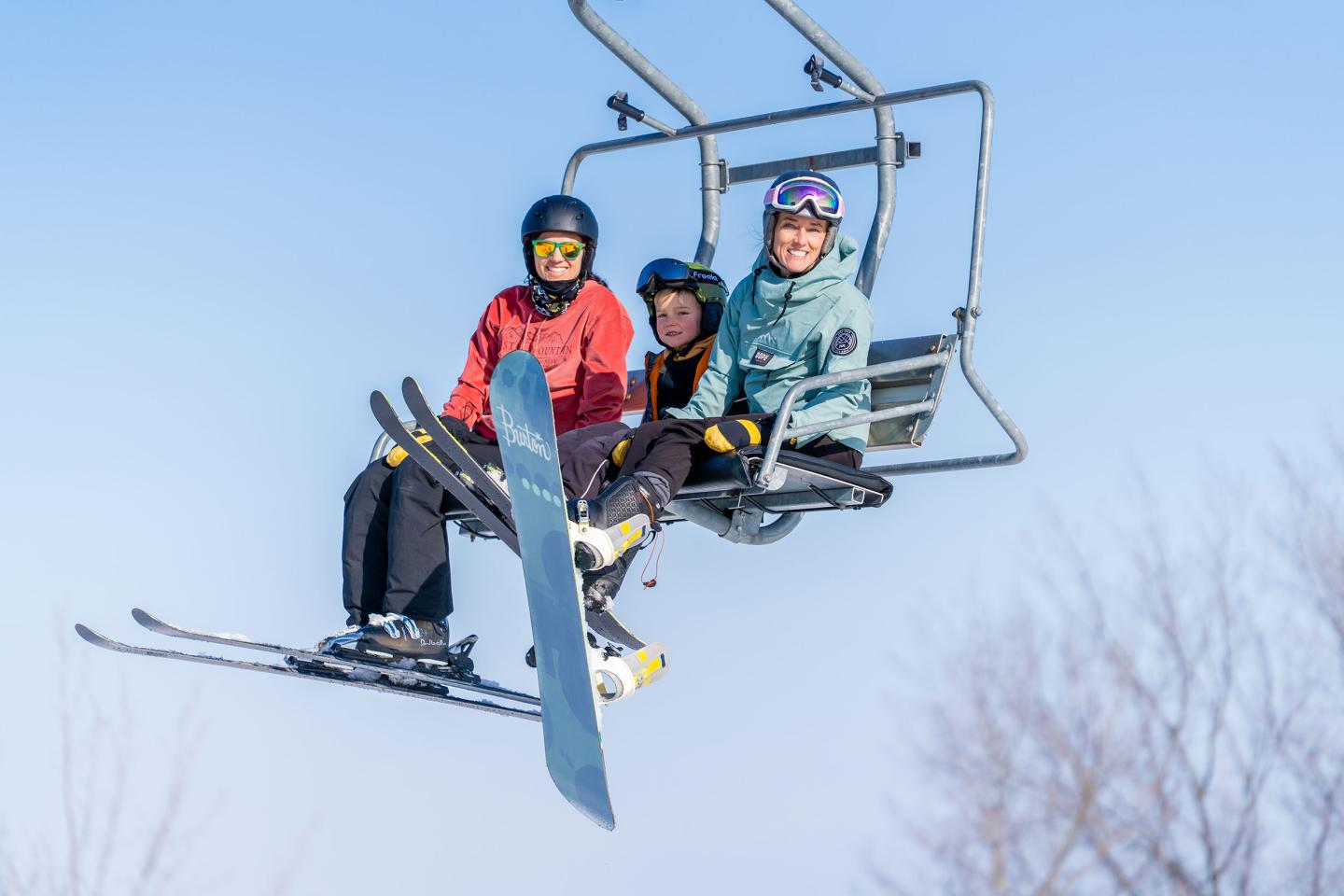 Three skiers on a ski lift against a blue sky.